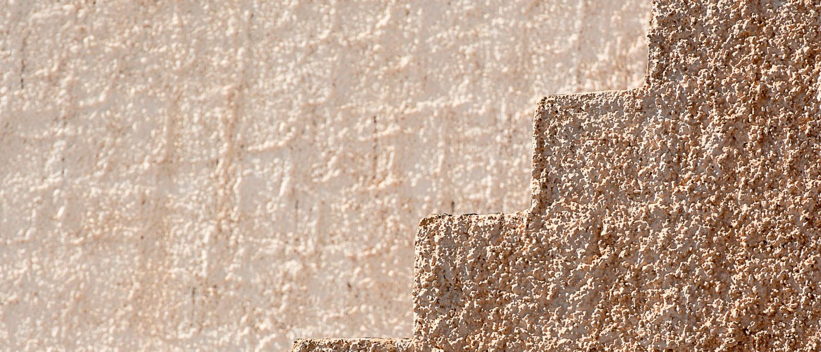 Mur maçonné en escalier recouvert d'un enduit à la chaux teinte sable