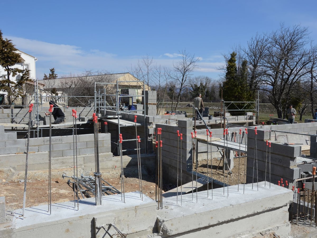 Fondations et premières assises de blocs d'une extension, étais et armatures en attente sur un chantier rangé