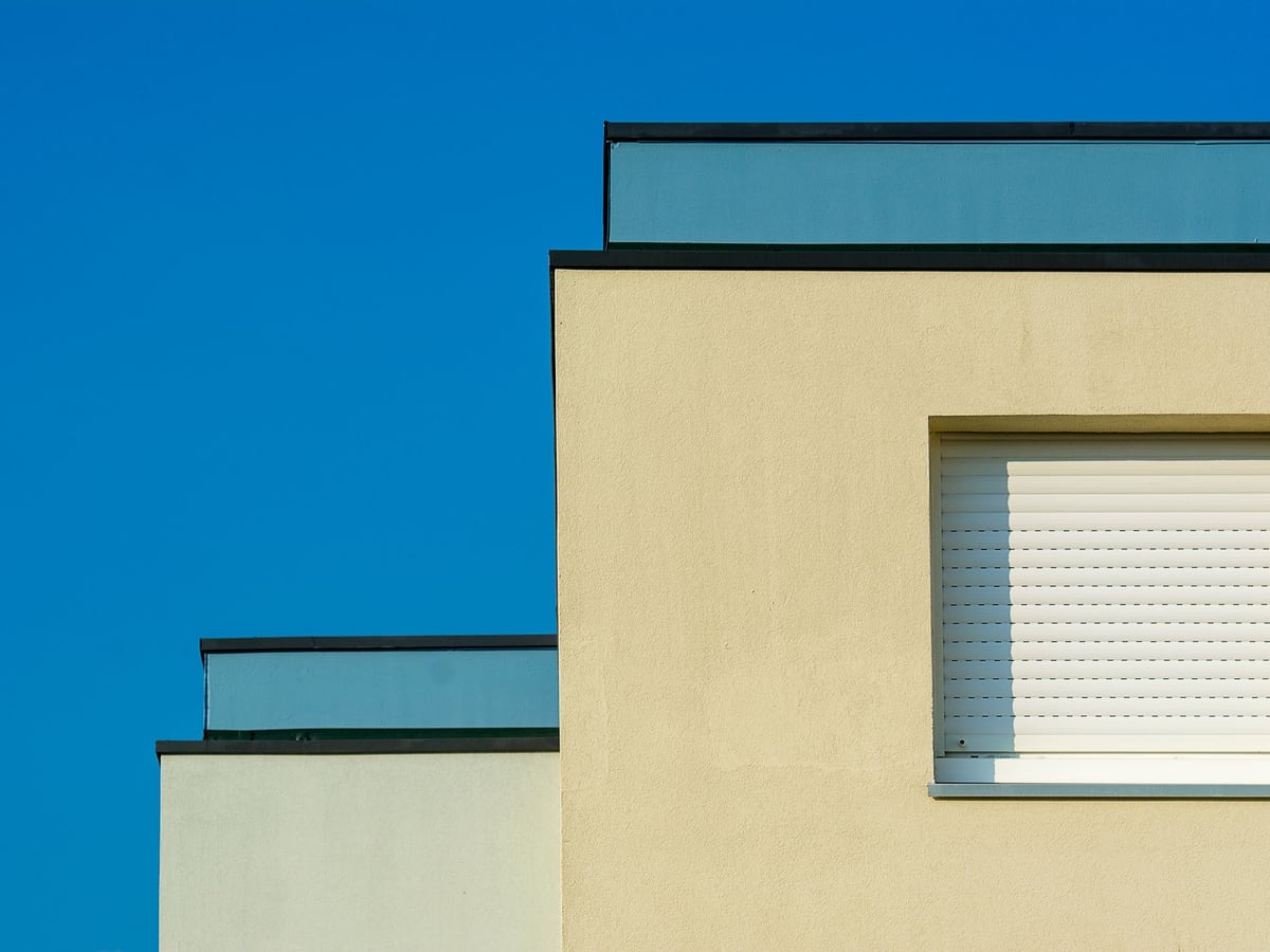 Façade enduite terminée dans une teinte claire, acrotères nets sous un ciel bleu